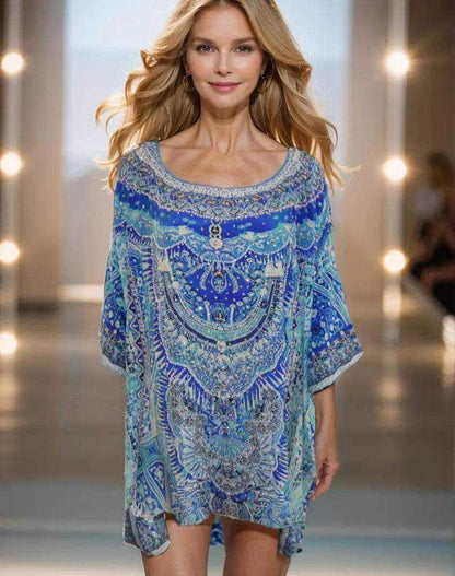 Woman wearing blue silk hi-low kaftan top with Egyptian-inspired embellishments.