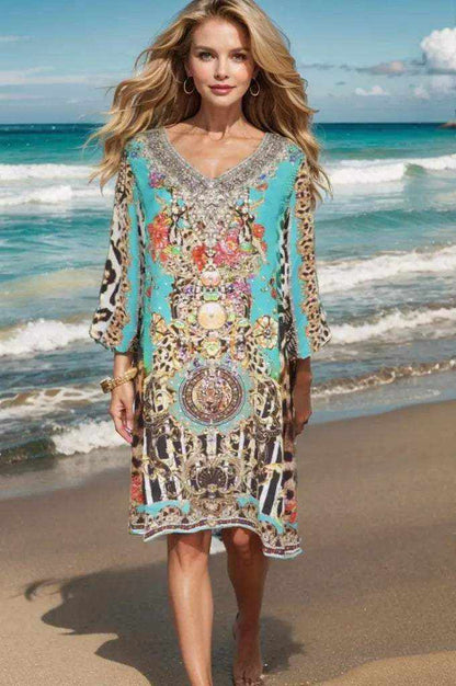 Woman wearing Garden Delight Aqua short silk embellished tunic dress walking on beach with ocean background