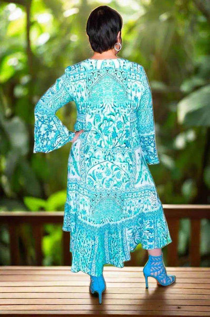 Woman wearing a turquoise patterned Silk hi-low Frill Dress with long sleeves and frilled hemline standing outdoors