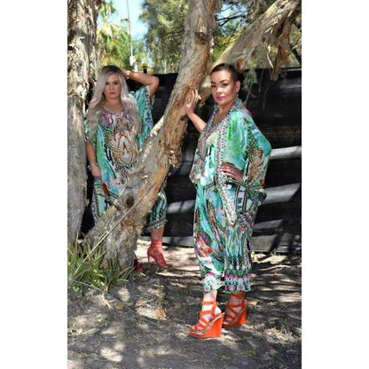 Women wearing Paradise green silk harem pants with colorful prints and hand-sewn beadwork, posing outdoors near trees