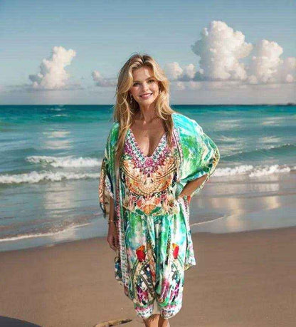Woman wearing Paradise green silk harem pants with colorful print and beadwork standing on beach with ocean and clouds in background