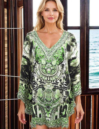 Woman wearing green silk embellished butterfly top with beadwork and V-neck standing indoors near window