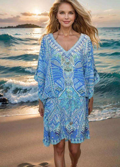 Woman wearing blue Short Silk Embellished Kaftan Geo with geometric patterns standing on beach at sunset