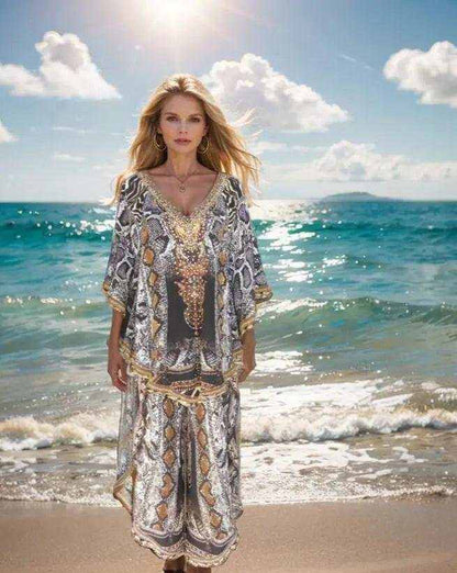 Woman wearing silk embellished butterfly top with snake print and beadwork standing on beach at sunrise