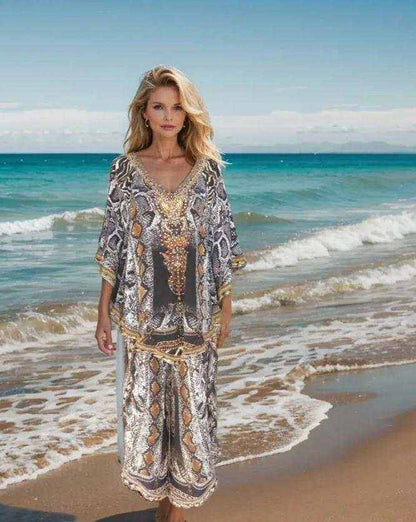 Woman wearing silk embellished butterfly top with snake print and beadwork standing on beach by ocean waves