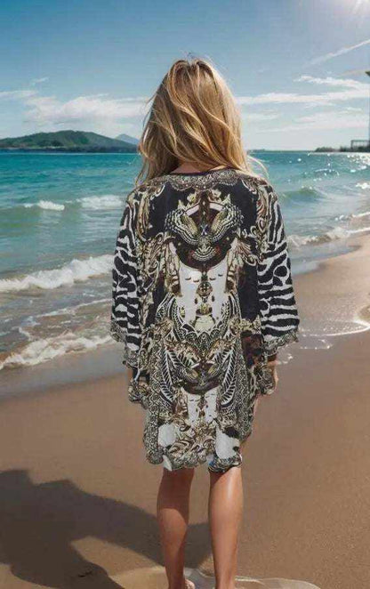 woman wearing silk embellished butterfly top with animal print and beadwork walking on beach