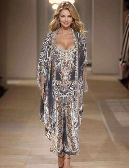 Model walking runway wearing silk embellished wrap pants with cobra snake print and handsewn beadwork matching silk top and short cape